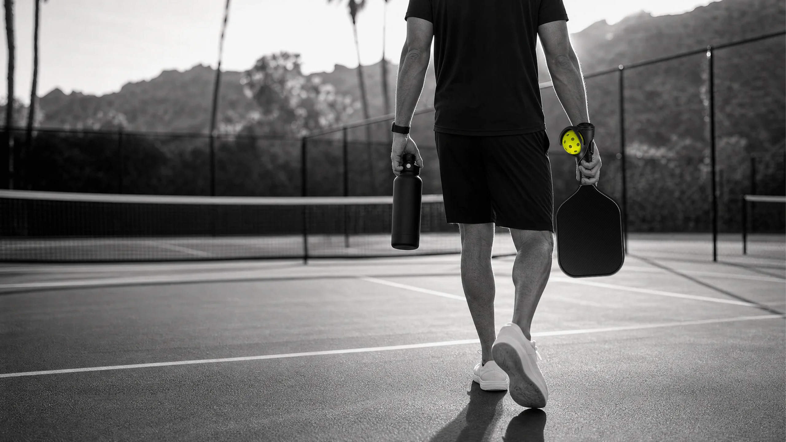 Pickleball player walking onto court carrying a paddle with PaddlePod ball holder and pickleball attached